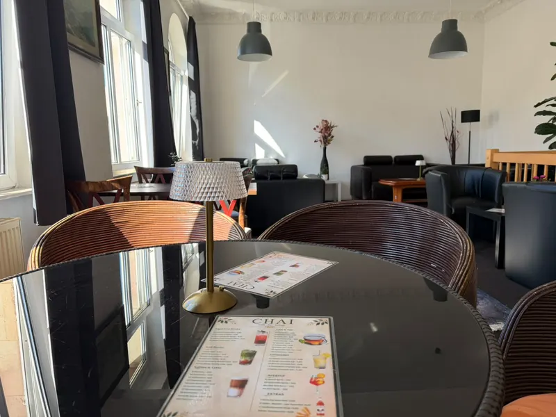 Runder Glastisch mit Rattansesseln, einer Tischlampe aus Messing und der Chai-Karte