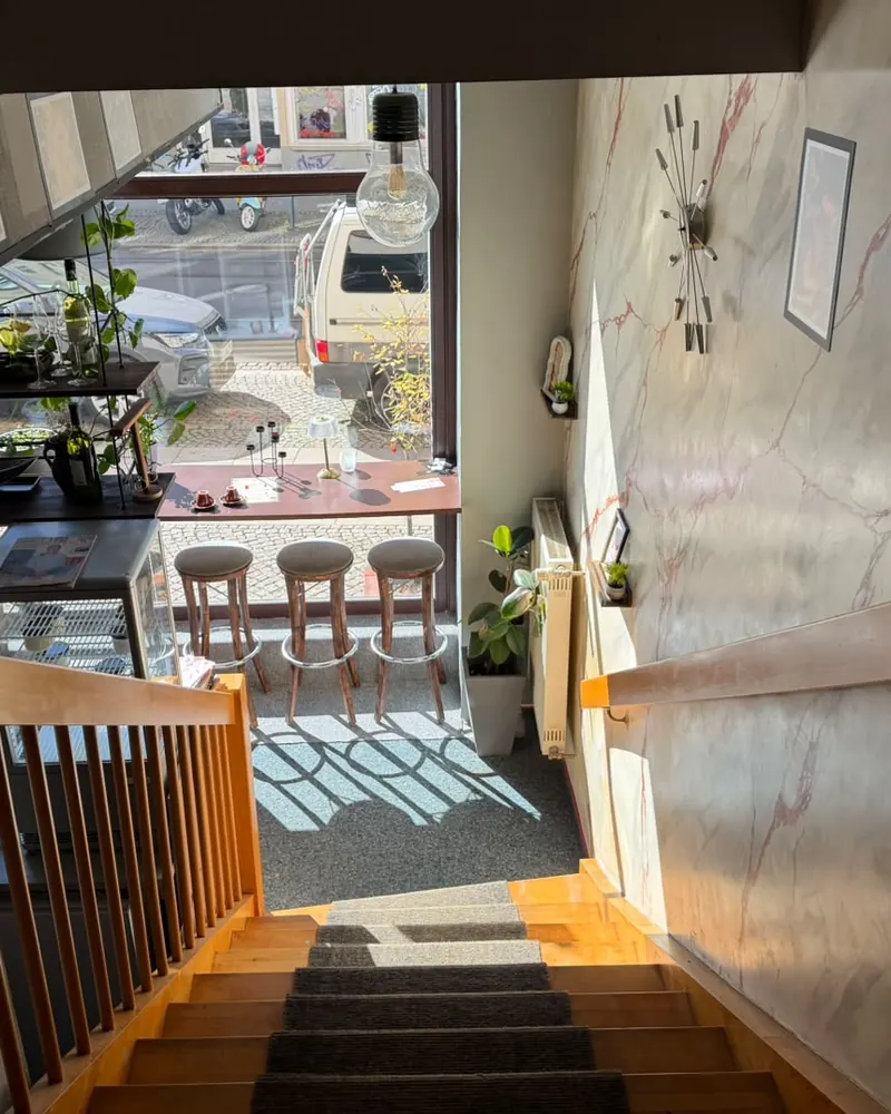 Blick die Treppe hinunter auf die Fensterbank mit drei Barhockern und die Straße davor